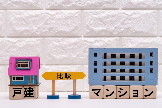 戸建てとマンションの模型が「比較」の看板をはさんで並ぶイメージ