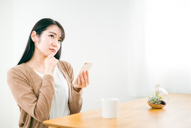 スマートフォンを手に、思案顔で考え込む女性