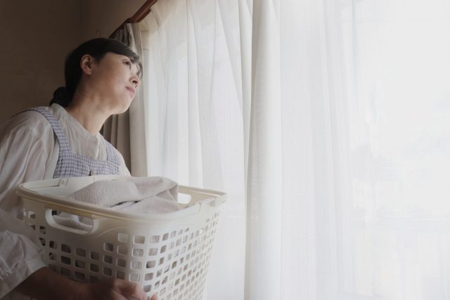 カーテンのそばで洗濯かごを持つ女性